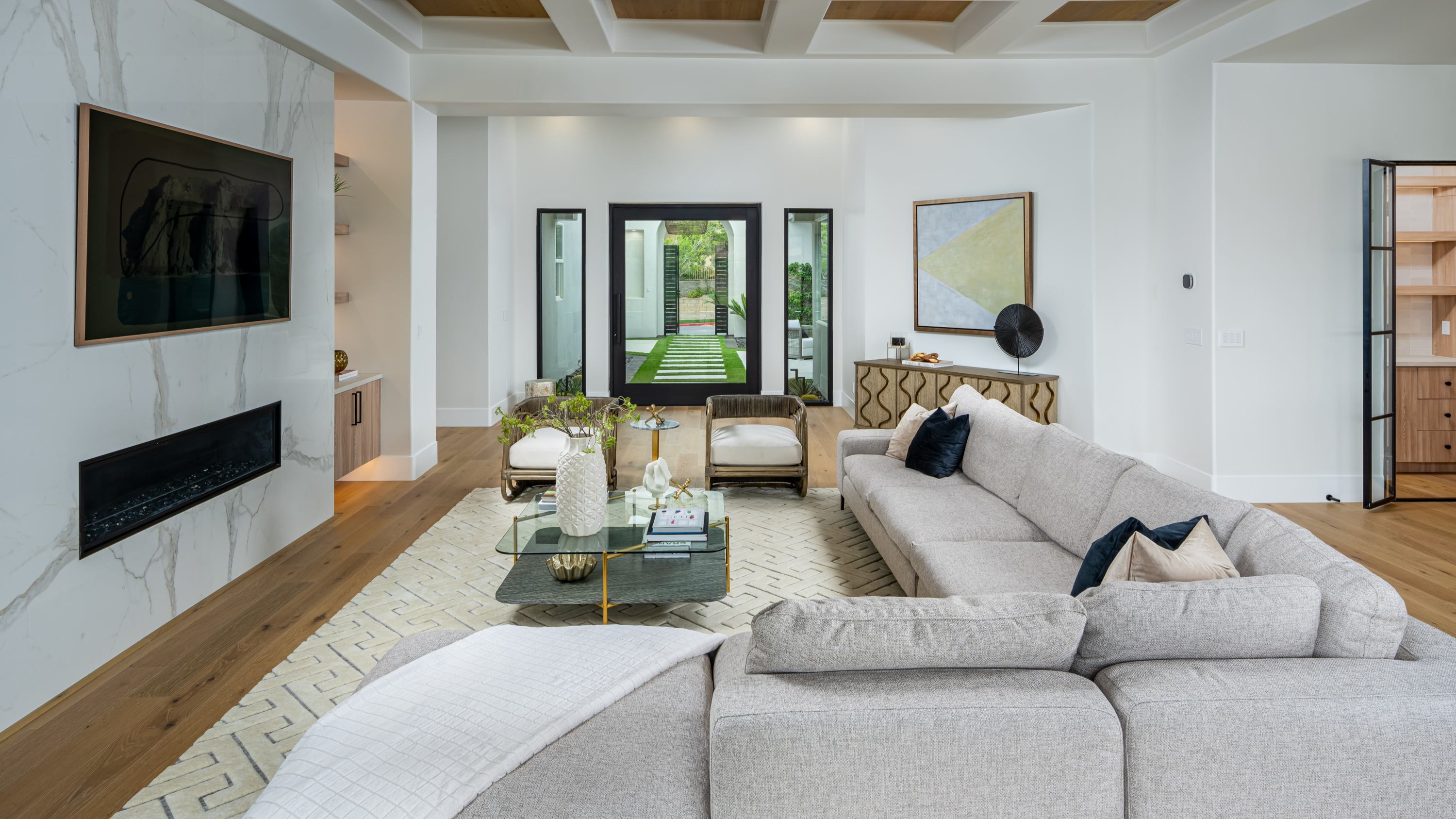 Spacious living room with coffered ceiling, neutral tones, a marble fireplace, and floor-to-ceiling windows with garden views.